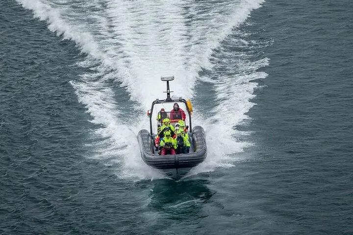 Ein RIB mit Gästen in gelben und roten Anzügen rast auf die Kamera zu und hinterlässt eine weiße Kielwelle